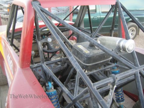 1990 Ford Bronco - Close-up of a red tube-chassis race truck's roll cage, fuel cell and blue coilover shocks viewed from the rear.