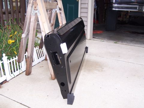 1986 Ford Bronco - A black vehicle door is propped up on sawhorses outside a garage, possibly awaiting repair or installation.
