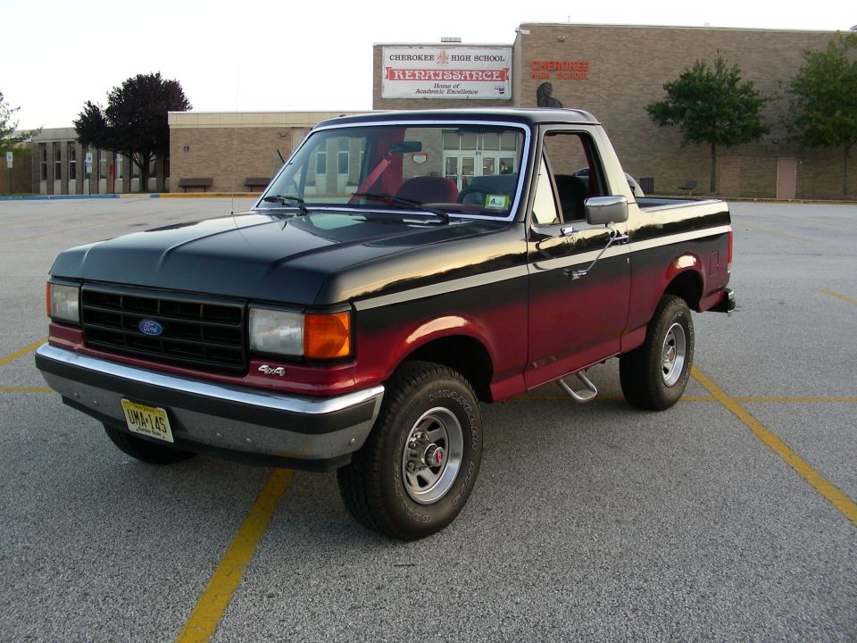 Black and red two-tone Ford Bronco with top removed, parked in a school parking lot