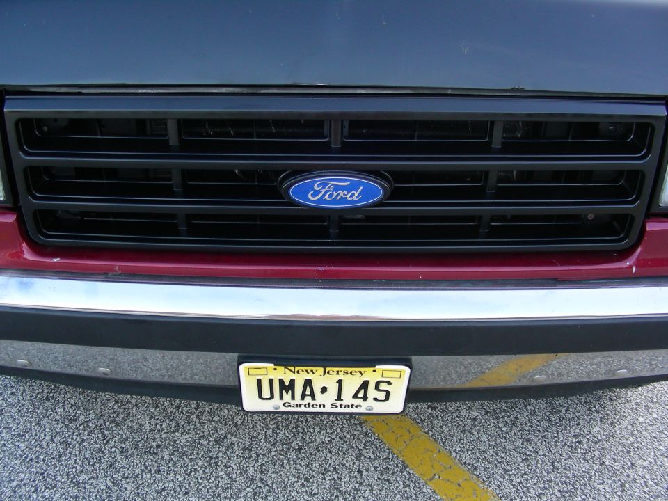 Black grille with blue Ford oval badge, red body panel, chrome bumper, and New Jersey license plate UMA-14S