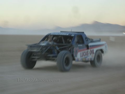 1990 Ford Bronco - Lucas Oil-sponsored number 17 off-road race truck speeds across a dusty desert flat at dusk.
