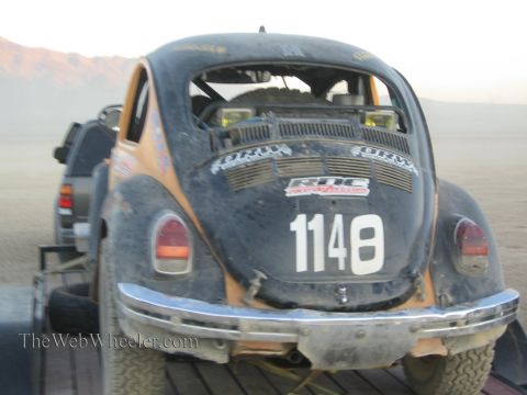 1990 Ford Bronco - dusty rear end of an orange Baja-style VW Beetle race car numbered 1148 sits on a trailer in the desert at dusk.