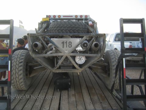 1990 Ford Bronco - Front view of a silver tube-chassis off-road race truck numbered 118, showing exposed engine and shocks, parked on a trailer.