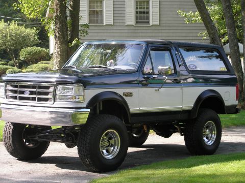 1994 Ford Bronco - This lifted Ford Bronco features a two-tone paint scheme and is parked on a driveway in front of a residential building.