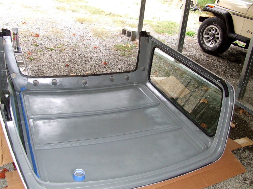 Gray primered Bronco hardtop resting upside down on cardboard in a carport