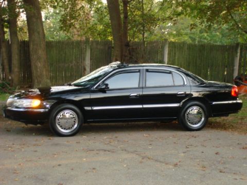 1997 Ford Crown Victoria - This black 1997 Lincoln Continental is parked on a dirt road with trees and a fence in the background.
