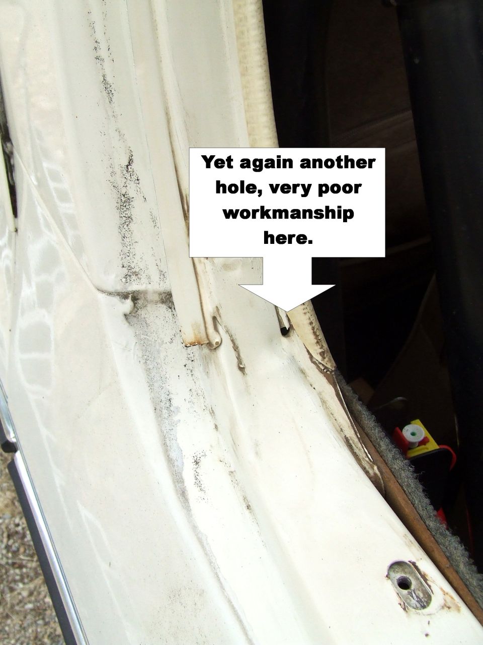 Rusty hole in a white body seam with caption arrow noting poor workmanship