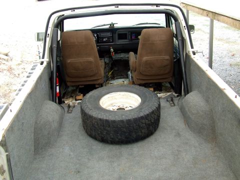 1979 Ford Bronco - The cargo bed and interior of a truck are visible, with a spare tire resting on the carpeted floor.