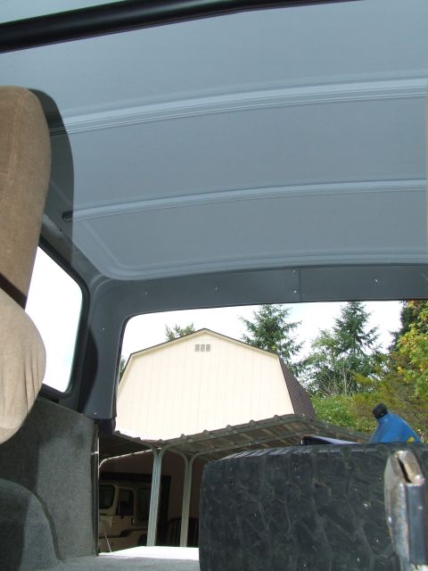 1979 Ford Bronco - View from inside a vehicle, looking out past a spare tire towards a barn and trees.