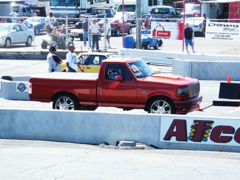 2001 Mercury Grand Marquis - A red pickup truck with custom wheels is parked at a drag strip, with racing numbers visible on the windshield.