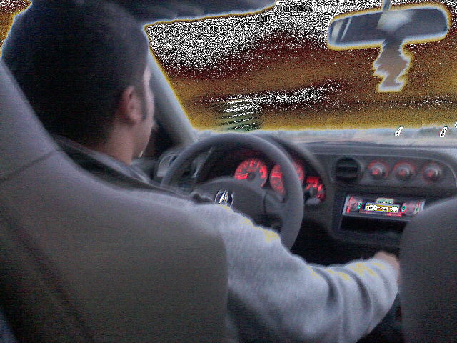 Interior view of a car with a driver, red illuminated gauges, and a car stereo