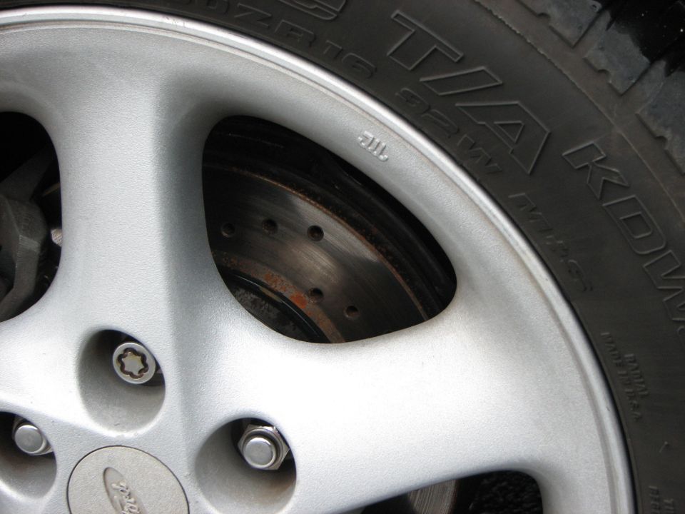 Close-up of a silver alloy wheel with a brake rotor visible behind it. Tire sidewall has TIA KOD markings