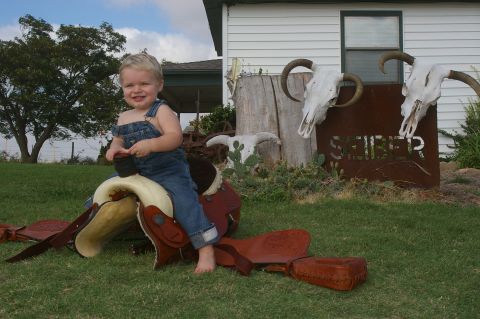 1998 Jeep TJ - A young child dressed in overalls sits atop a saddle, with a rustic outdoor scene cow skulls and a metal sign behind them.