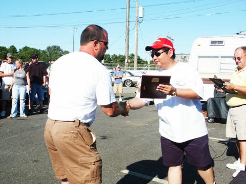 2001 Mercury Grand Marquis - Two men exchange awards at an outdoor car show, with other attendees and vehicles visible in the background.