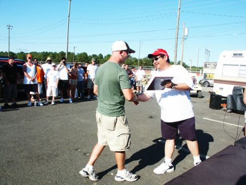2001 Mercury Grand Marquis - Two men shake hands at an outdoor car show, with spectators and vehicles visible in the background under a clear blue sky.
