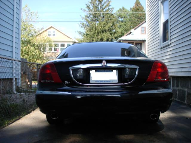 Black Lincoln Continental sedan, rear view, parked in driveway between houses