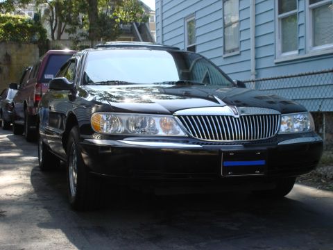1997 Ford Crown Victoria - A black Lincoln Continental is parked in front of a blue house, with other vehicles behind it.