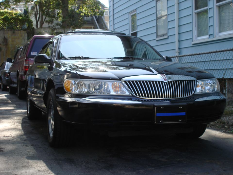 Black Lincoln Continental with chrome grille, parked in front of a blue house