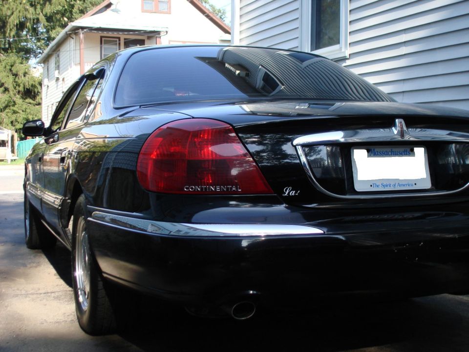 Black Lincoln Continental parked in driveway, rear view showing taillights and license plate
