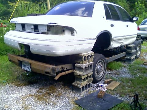 2002 Ford Crown Victoria - This Mercury Grand Marquis is elevated on cinder blocks, revealing its undercarriage and missing rear bumper.