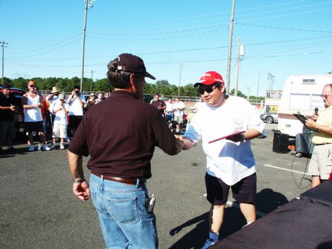 2001 Mercury Grand Marquis - Attendees interact at an outdoor car show event, with vehicles and a trailer visible in the background under a clear sky.