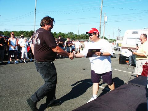 2001 Mercury Grand Marquis - Two men shake hands at an outdoor event, possibly a car show, with spectators and a trailer visible.