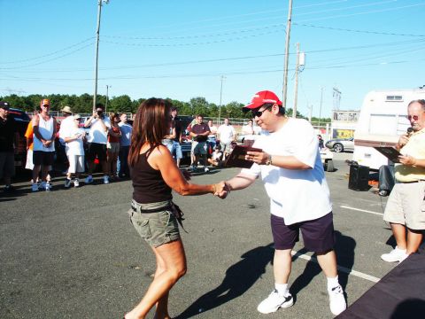 2001 Mercury Grand Marquis - A man presents an award to a woman at an outdoor event, with spectators and vehicles visible.