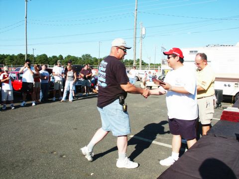 2001 Mercury Grand Marquis - Two men shake hands as an award is presented at an outdoor event with vehicles and spectators.