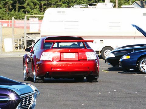 2001 Mercury Grand Marquis - A red sports car with a large rear spoiler is parked at a car show, with other vehicles visible.