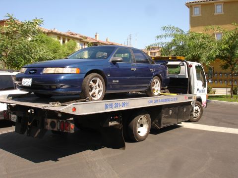 1992 Ford Taurus - A blue sedan with a rear spoiler is being transported on a tow truck.
