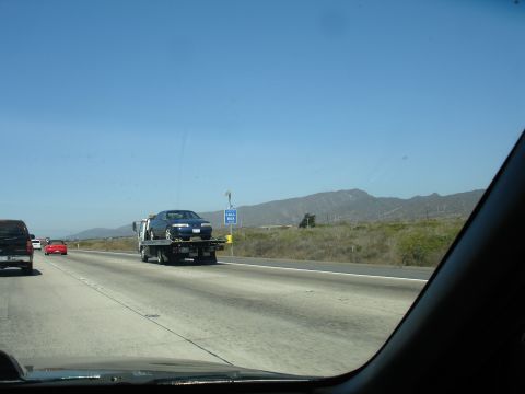 1992 Ford Taurus - A car is being transported on a tow truck along a highway under a clear blue sky.