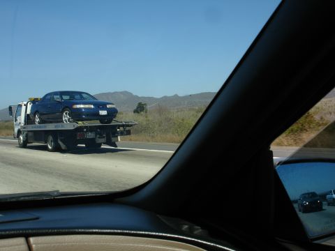 1992 Ford Taurus - A blue 1992 Ford Taurus is transported on a tow truck along a highway.
