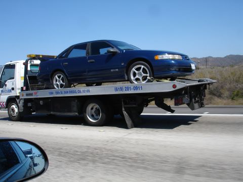 1992 Ford Taurus - A blue sedan is loaded onto a tow truck on a highway.