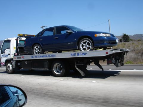 1992 Ford Taurus - A blue sedan is transported on a tow truck, with visible text on the truck indicating "Precision" and a phone number.