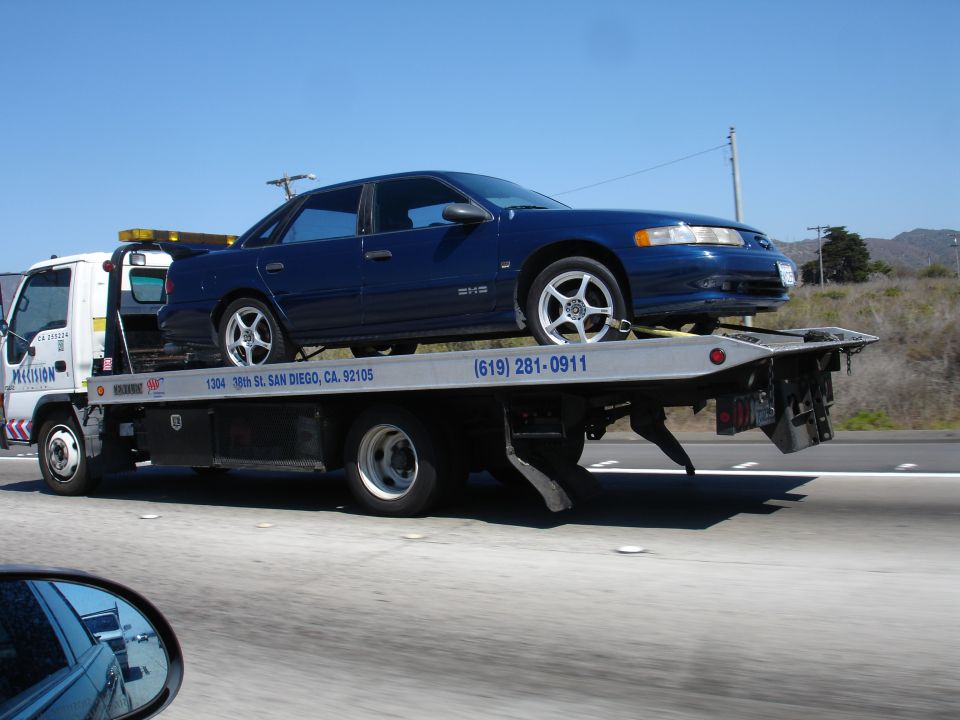 Blue sedan on a flatbed tow truck, side view, with "Precision" and phone number visible on the truck
