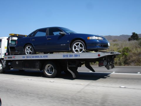 1992 Ford Taurus - A blue 1992 Ford Taurus is transported on a tow truck along a highway.
