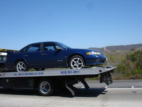 1992 Ford Taurus - Blue 1992 Ford Taurus being transported on a flatbed tow truck on a highway.