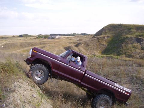 1979 Ford F-250 - A lifted pickup truck navigates a steep, grassy incline under a cloudy sky.