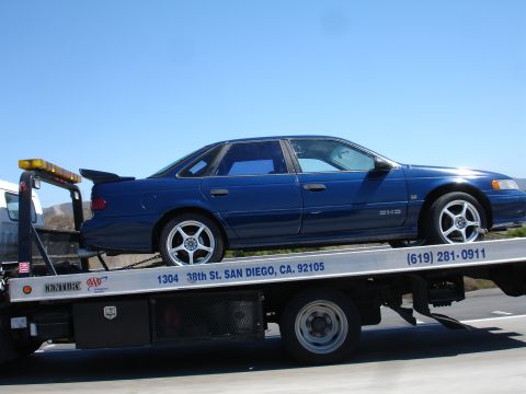 1992 Ford Taurus - A blue sedan is being towed on a flatbed truck under a clear blue sky.
