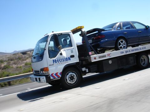 1992 Ford Taurus - A blue 1992 Ford Taurus is loaded onto a tow truck on a sunny day.