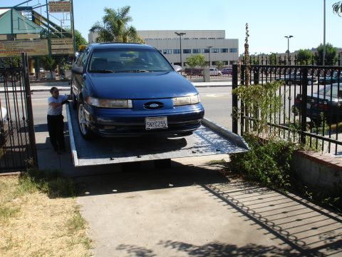 1992 Ford Taurus - A blue 1992 Ford Taurus is loaded onto a tow truck, viewed from the front.
