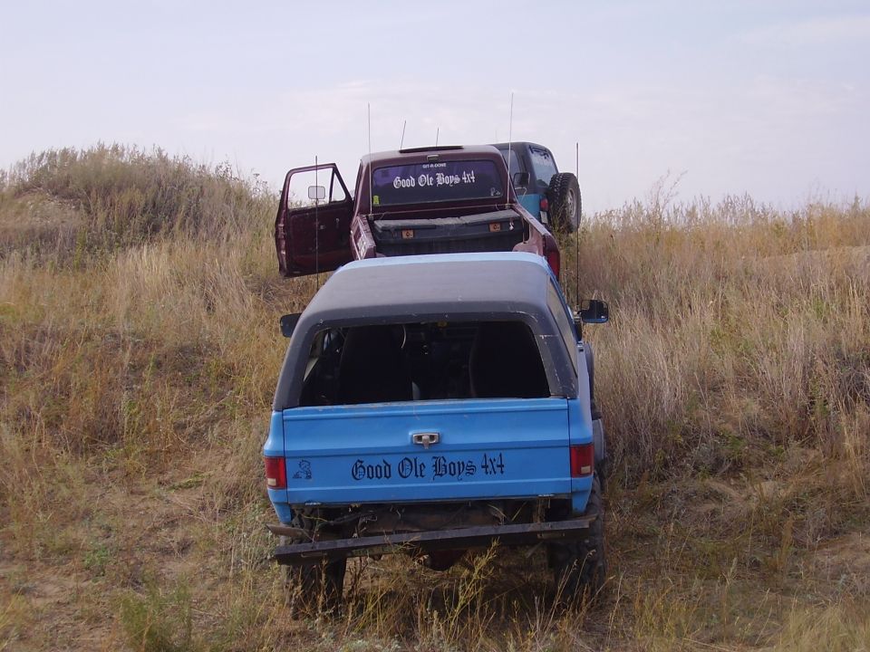 Blue SUV and maroon pickup truck parked on a grassy hill. Both have 'Good Ole Boys 4x4' decals