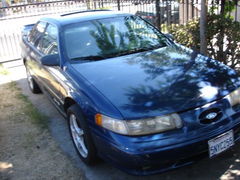 1992 Ford Taurus - A blue 1992 Ford Taurus is parked in a driveway, a sunroof and a clear view of its front end.