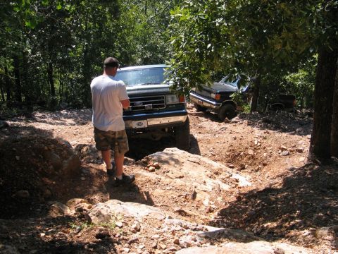 1990 Ford Bronco - Two Ford Broncos tackling an off-road trail with a person standing by the lead vehicle.