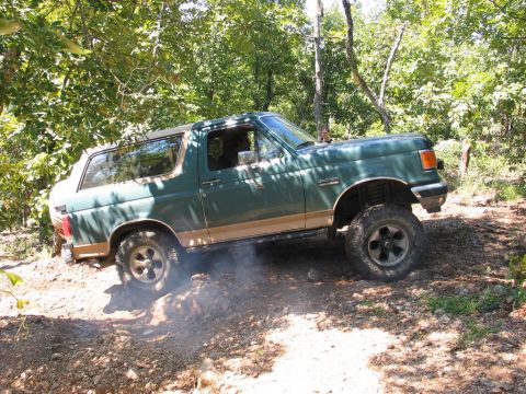 1990 Ford Bronco - A green Ford Bronco navigates a dirt trail with trees in the background.