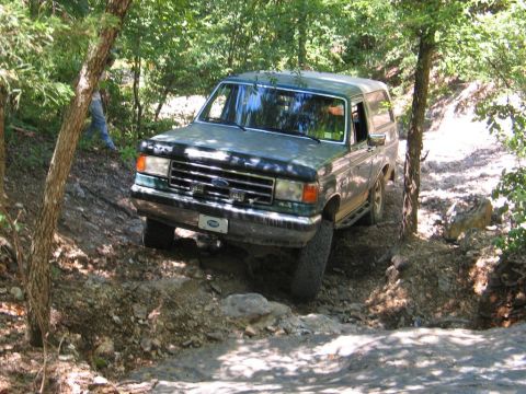 1990 Ford Bronco - This 1990 Ford Bronco is shown tackling a challenging off-road trail with steep inclines and rocky obstacles.
