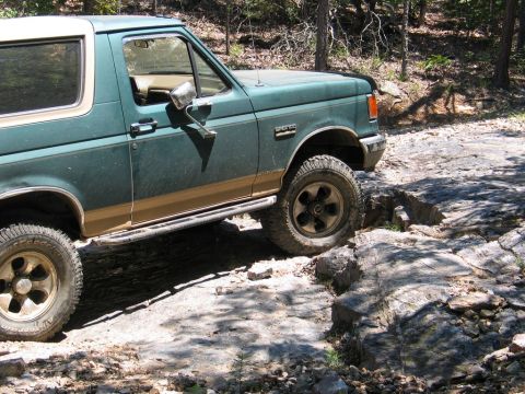 1990 Ford Bronco - Ford Bronco navigating a challenging rocky path in a wooded area.