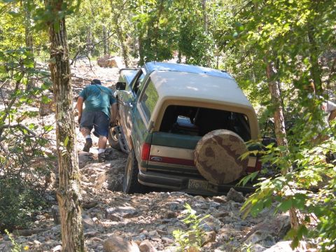 1990 Ford Bronco - A Ford Bronco navigates a challenging, rocky off-road path with assistance from a spotter.