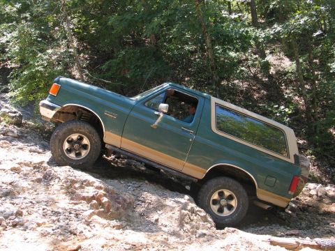 1990 Ford Bronco - A green Ford Bronco navigates a challenging rocky trail off-road.