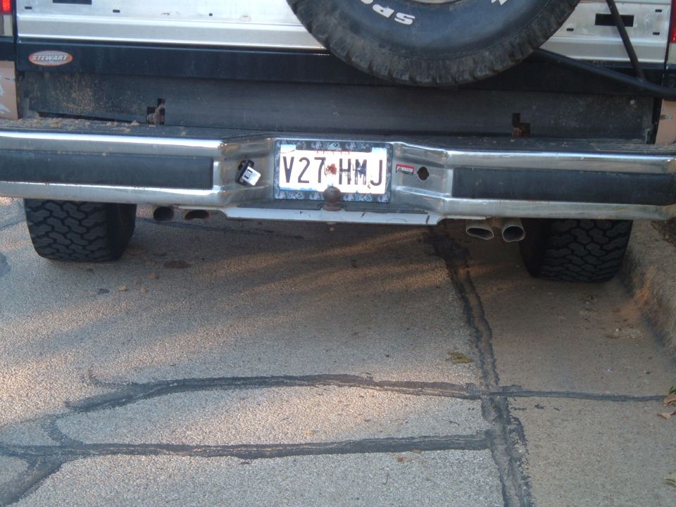 Rear bumper and license plate V27 HMJ on lifted truck with spare tire and dual exhaust on pavement